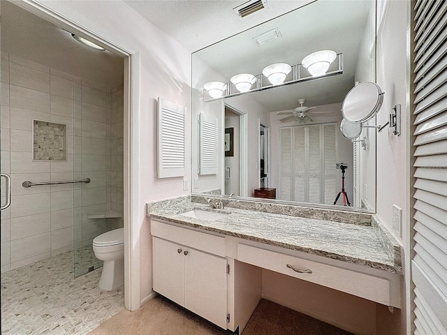 bathroom featuring ceiling fan, a textured ceiling, toilet, vanity, and a shower with shower door