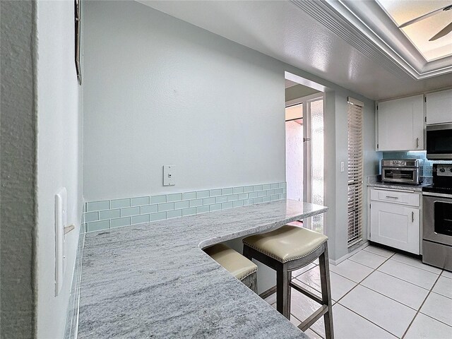 kitchen featuring decorative backsplash, white cabinetry, light tile patterned floors, and stainless steel appliances