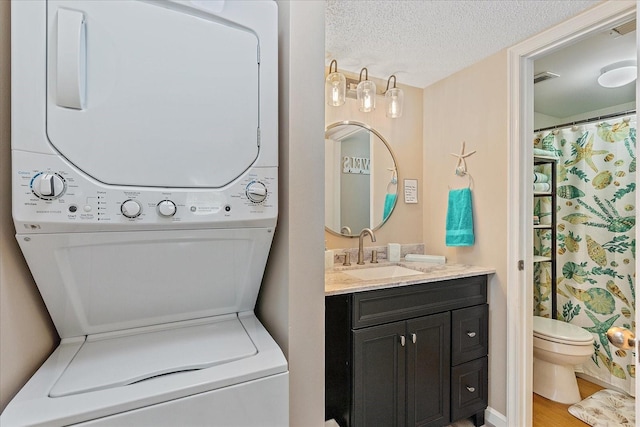 clothes washing area with a textured ceiling, sink, hardwood / wood-style floors, and stacked washer and clothes dryer