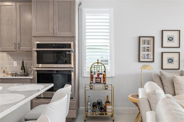 kitchen with tasteful backsplash, light stone counters, light tile patterned floors, and stainless steel double oven