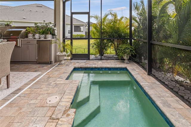 view of pool with exterior kitchen, glass enclosure, a patio area, and a grill