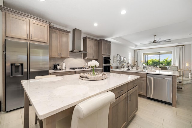 kitchen featuring light stone countertops, appliances with stainless steel finishes, ceiling fan, wall chimney range hood, and a center island