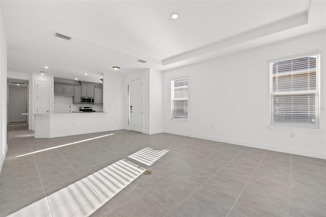 unfurnished living room featuring a raised ceiling and light tile patterned floors