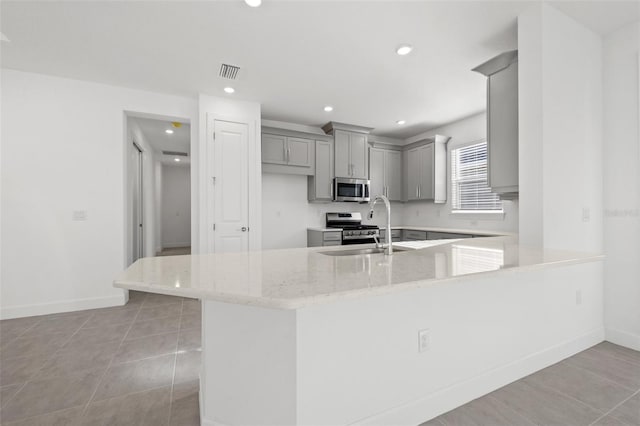 kitchen with sink, light stone counters, appliances with stainless steel finishes, gray cabinets, and kitchen peninsula