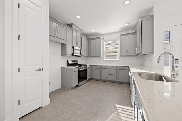 kitchen featuring sink, gray cabinetry, light stone counters, light tile patterned floors, and appliances with stainless steel finishes