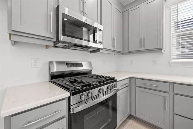 kitchen featuring stainless steel appliances, gray cabinets, light tile patterned floors, and light stone counters