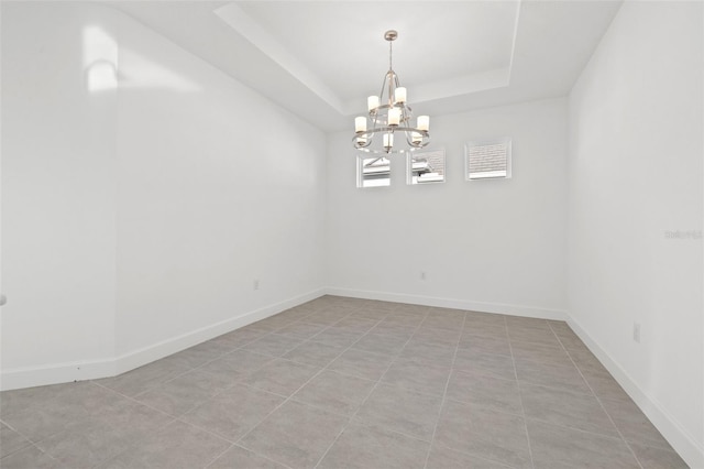 tiled spare room with a notable chandelier and a tray ceiling