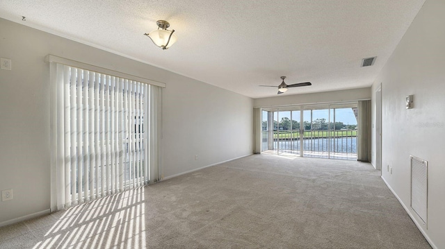 carpeted spare room featuring ceiling fan, a water view, and a textured ceiling