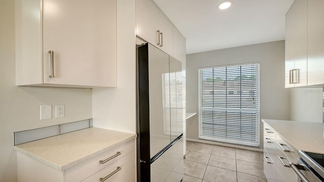 kitchen featuring stove, light stone counters, high end fridge, white cabinetry, and light tile patterned flooring