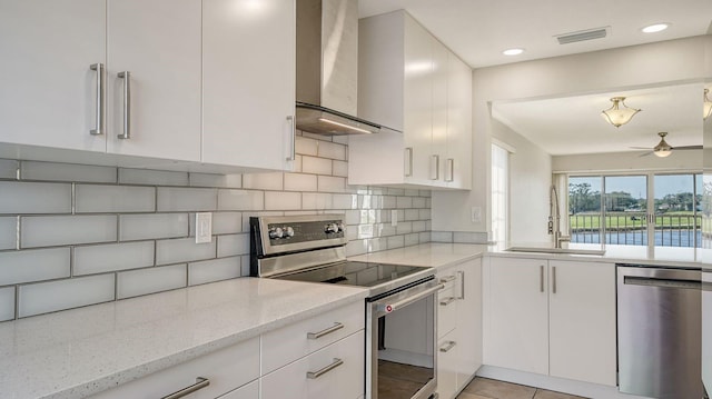 kitchen with tasteful backsplash, light stone counters, stainless steel appliances, sink, and wall chimney range hood