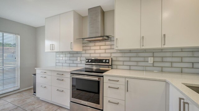 kitchen with stainless steel range with electric cooktop, wall chimney range hood, decorative backsplash, light stone counters, and white cabinetry