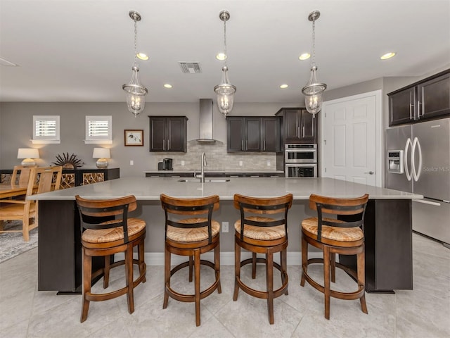 kitchen featuring appliances with stainless steel finishes, dark brown cabinetry, wall chimney exhaust hood, and a spacious island