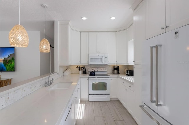 kitchen with white cabinetry, sink, hanging light fixtures, and white appliances