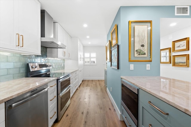 kitchen featuring tasteful backsplash, white cabinetry, wall chimney exhaust hood, and appliances with stainless steel finishes