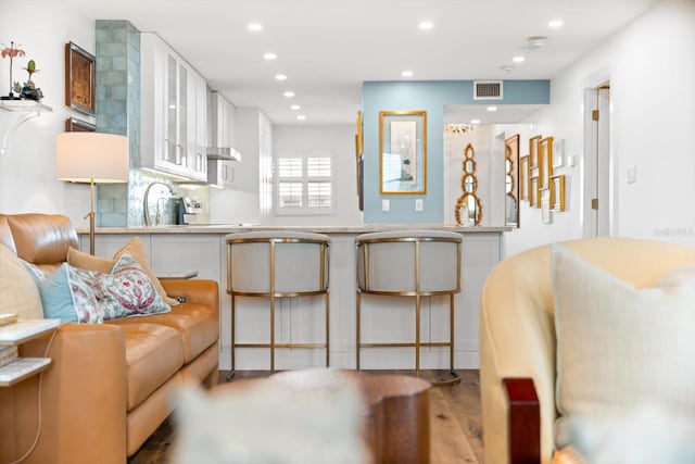 kitchen with a kitchen breakfast bar, sink, decorative backsplash, light hardwood / wood-style floors, and white cabinetry