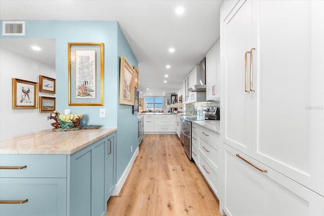 kitchen featuring stainless steel range with electric stovetop, light hardwood / wood-style flooring, wall chimney exhaust hood, light stone counters, and white cabinetry