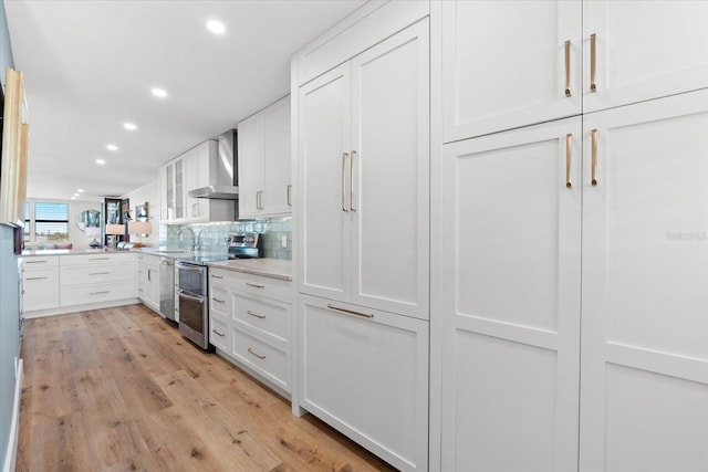 kitchen with white cabinets, wall chimney range hood, tasteful backsplash, light hardwood / wood-style floors, and stainless steel appliances