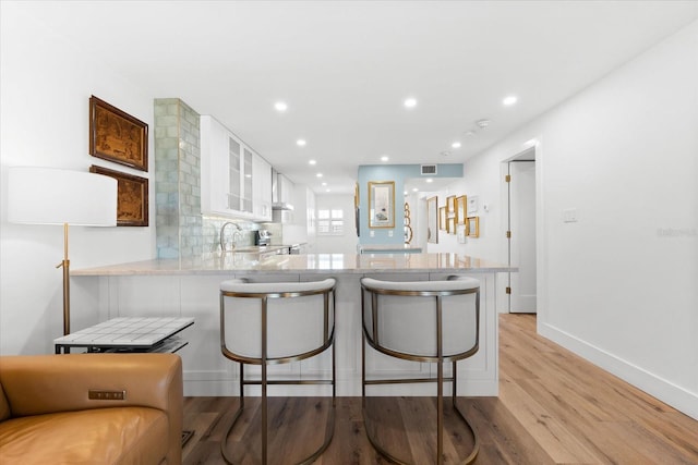 kitchen with white cabinets, light wood-type flooring, kitchen peninsula, and a breakfast bar area