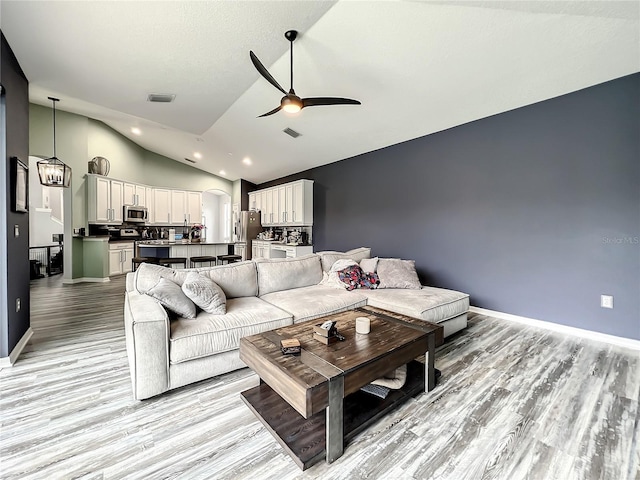 living room with ceiling fan with notable chandelier, light hardwood / wood-style floors, and lofted ceiling