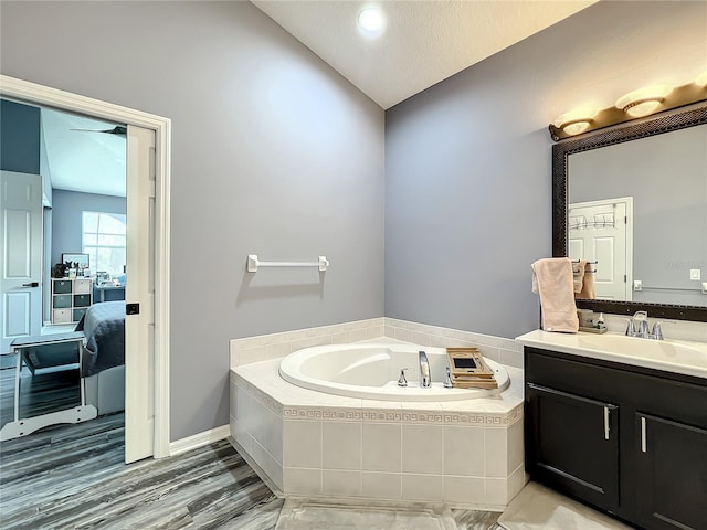 bathroom with hardwood / wood-style flooring, vanity, a relaxing tiled tub, and vaulted ceiling