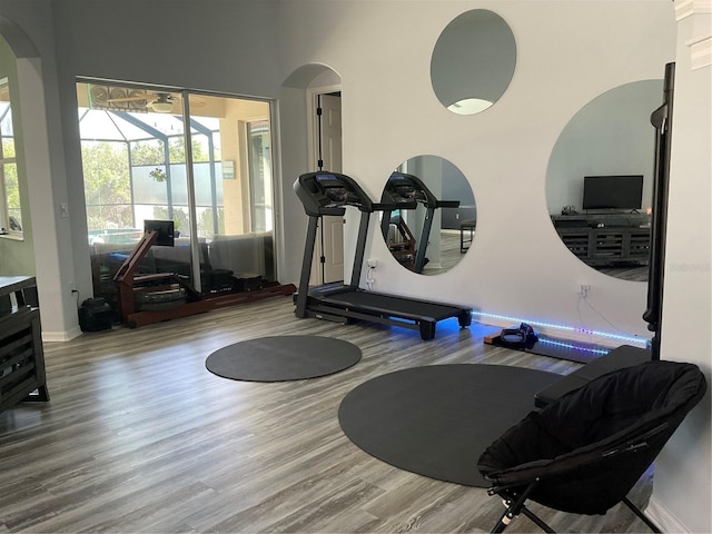 exercise room with arched walkways, wood finished floors, and baseboards