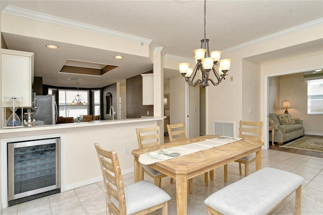 tiled dining room featuring a textured ceiling, crown molding, wine cooler, and an inviting chandelier