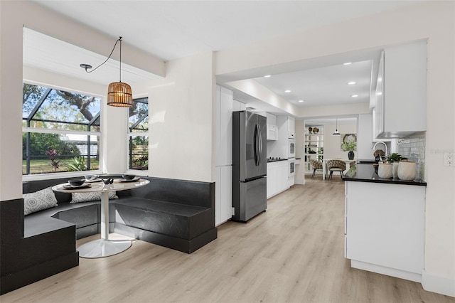 kitchen featuring breakfast area, hanging light fixtures, stainless steel fridge, light hardwood / wood-style floors, and white cabinetry