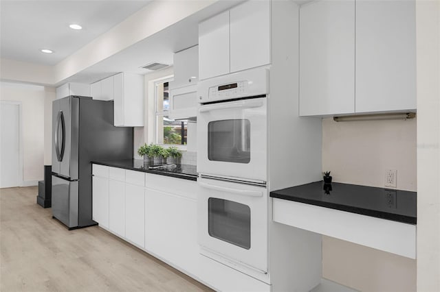 kitchen featuring white cabinets, stainless steel fridge, light wood-type flooring, and double oven