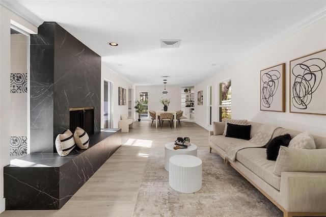 living room featuring built in shelves, light hardwood / wood-style floors, ornamental molding, and a high end fireplace