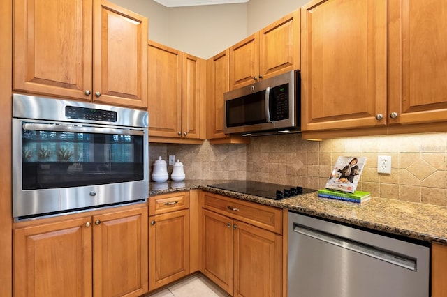 kitchen featuring dark stone counters, light tile patterned floors, appliances with stainless steel finishes, and decorative backsplash