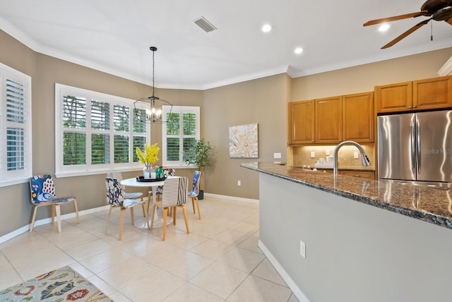 kitchen with dark stone countertops, light tile patterned floors, pendant lighting, and stainless steel fridge