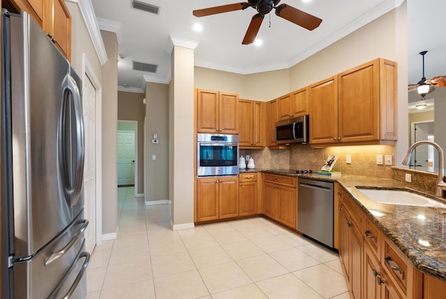 kitchen with appliances with stainless steel finishes, dark stone countertops, sink, light tile patterned floors, and crown molding