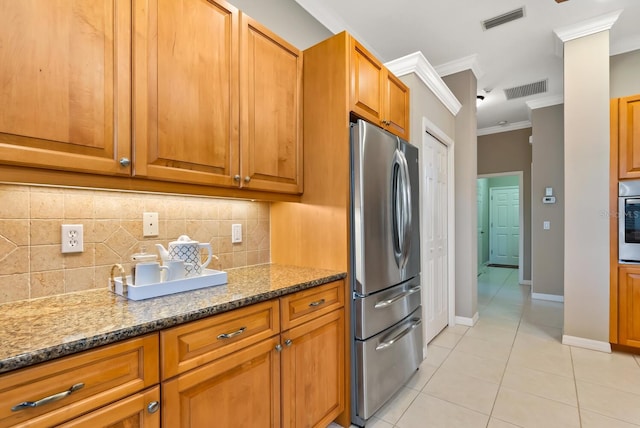 kitchen featuring appliances with stainless steel finishes, light tile patterned floors, ornamental molding, backsplash, and dark stone counters