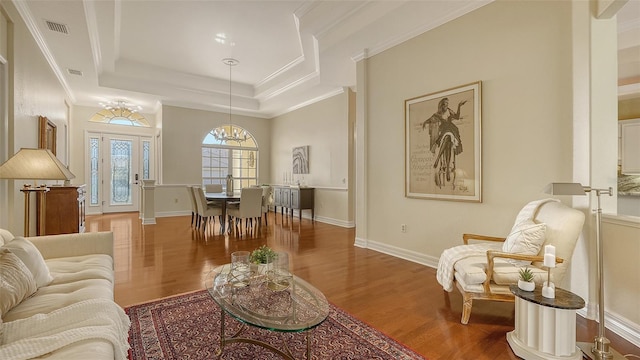 living room featuring wood-type flooring, a tray ceiling, ornamental molding, and a notable chandelier