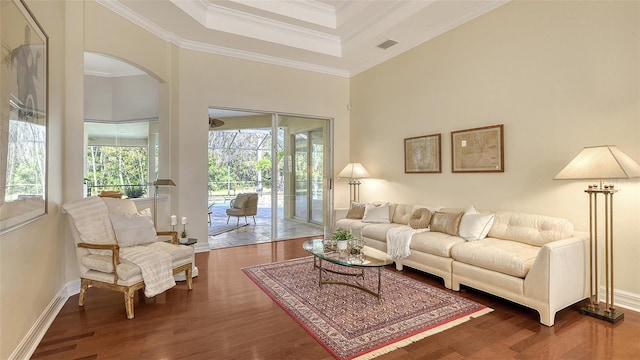 living room with a towering ceiling, dark wood-type flooring, a raised ceiling, and crown molding