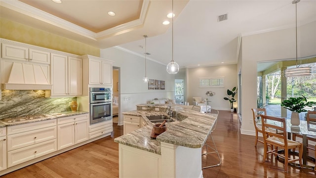 kitchen with sink, hanging light fixtures, a kitchen island with sink, appliances with stainless steel finishes, and custom exhaust hood