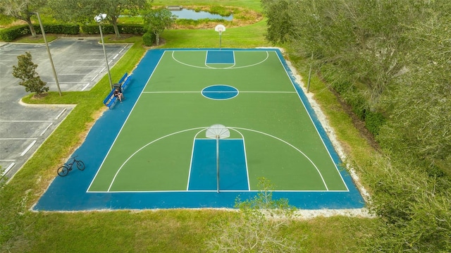 view of sport court with a water view and a lawn