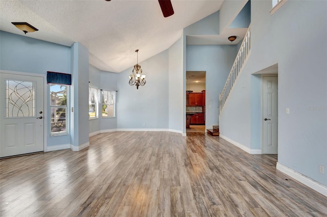 interior space featuring ceiling fan with notable chandelier, light wood-type flooring, a textured ceiling, and high vaulted ceiling