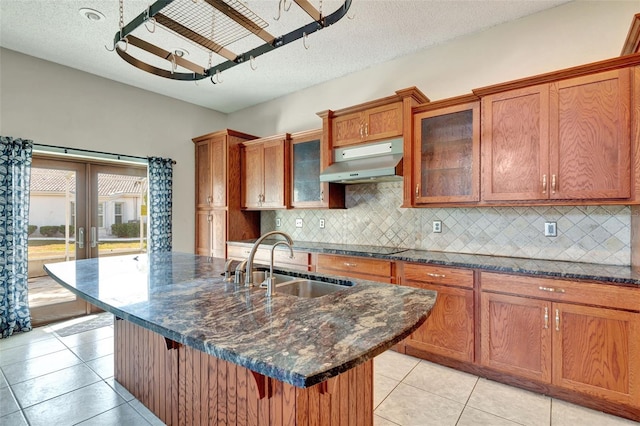 kitchen with sink, tasteful backsplash, an island with sink, a breakfast bar, and light tile patterned floors