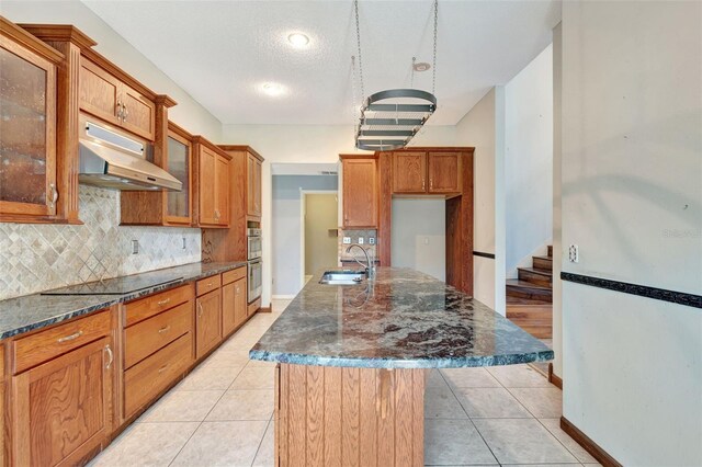 kitchen with a center island with sink, black electric stovetop, sink, decorative backsplash, and light tile patterned floors