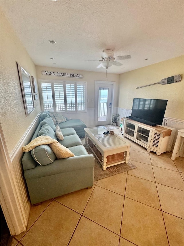 living room featuring a wainscoted wall, a textured wall, a ceiling fan, a textured ceiling, and tile patterned floors