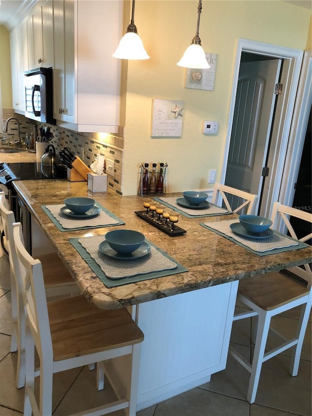 kitchen with a sink, white cabinets, a kitchen breakfast bar, appliances with stainless steel finishes, and backsplash