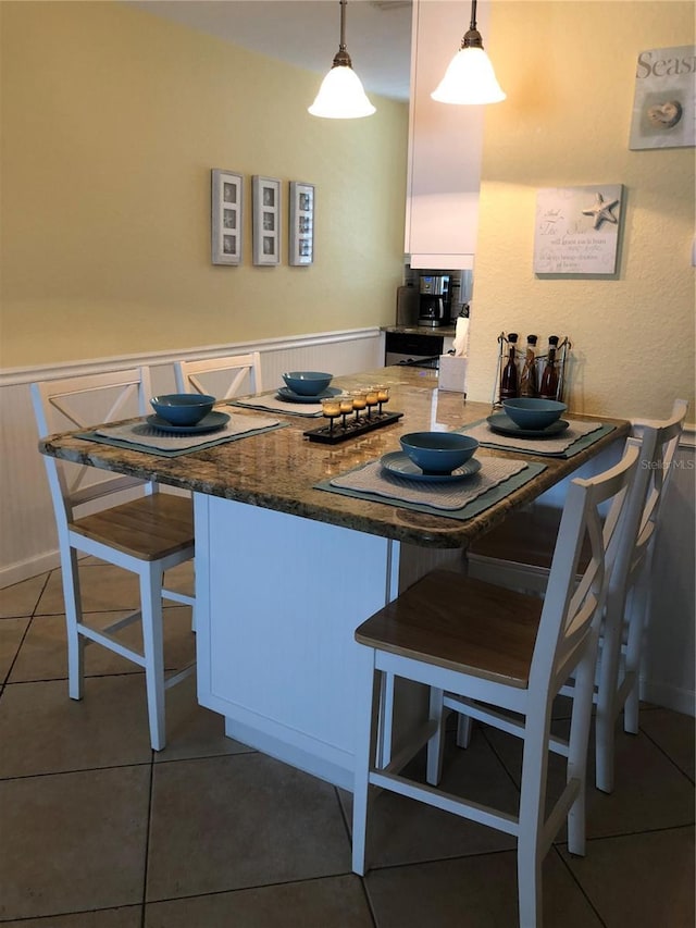 kitchen with tile patterned flooring, white cabinetry, a kitchen breakfast bar, hanging light fixtures, and wainscoting