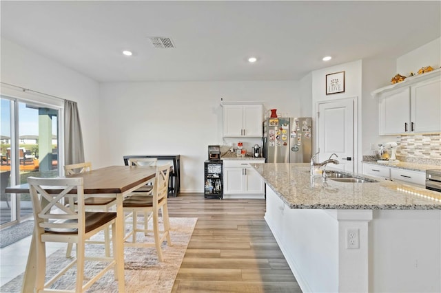 kitchen featuring light stone countertops, sink, stainless steel fridge, an island with sink, and white cabinets