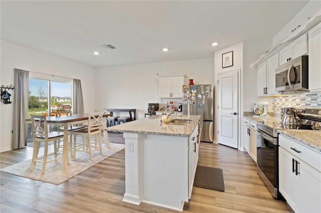 kitchen with light stone countertops, stainless steel appliances, a kitchen island with sink, sink, and white cabinetry