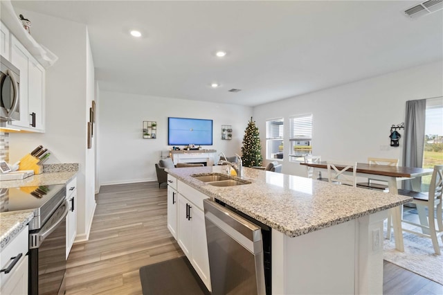 kitchen with white cabinetry, sink, stainless steel appliances, an island with sink, and light hardwood / wood-style floors