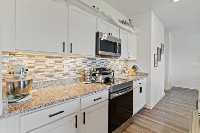 kitchen with light stone countertops, white cabinetry, stainless steel appliances, tasteful backsplash, and light hardwood / wood-style floors