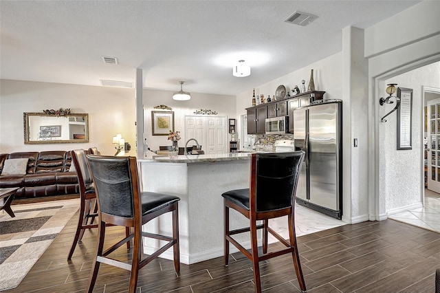 kitchen featuring a kitchen breakfast bar, light stone countertops, dark brown cabinets, kitchen peninsula, and stainless steel appliances