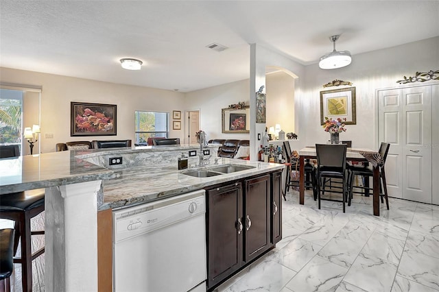 kitchen featuring light stone counters, dark brown cabinets, sink, dishwasher, and a breakfast bar area