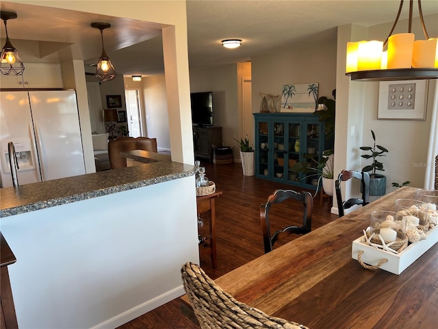 kitchen with pendant lighting, white refrigerator with ice dispenser, and dark wood-type flooring